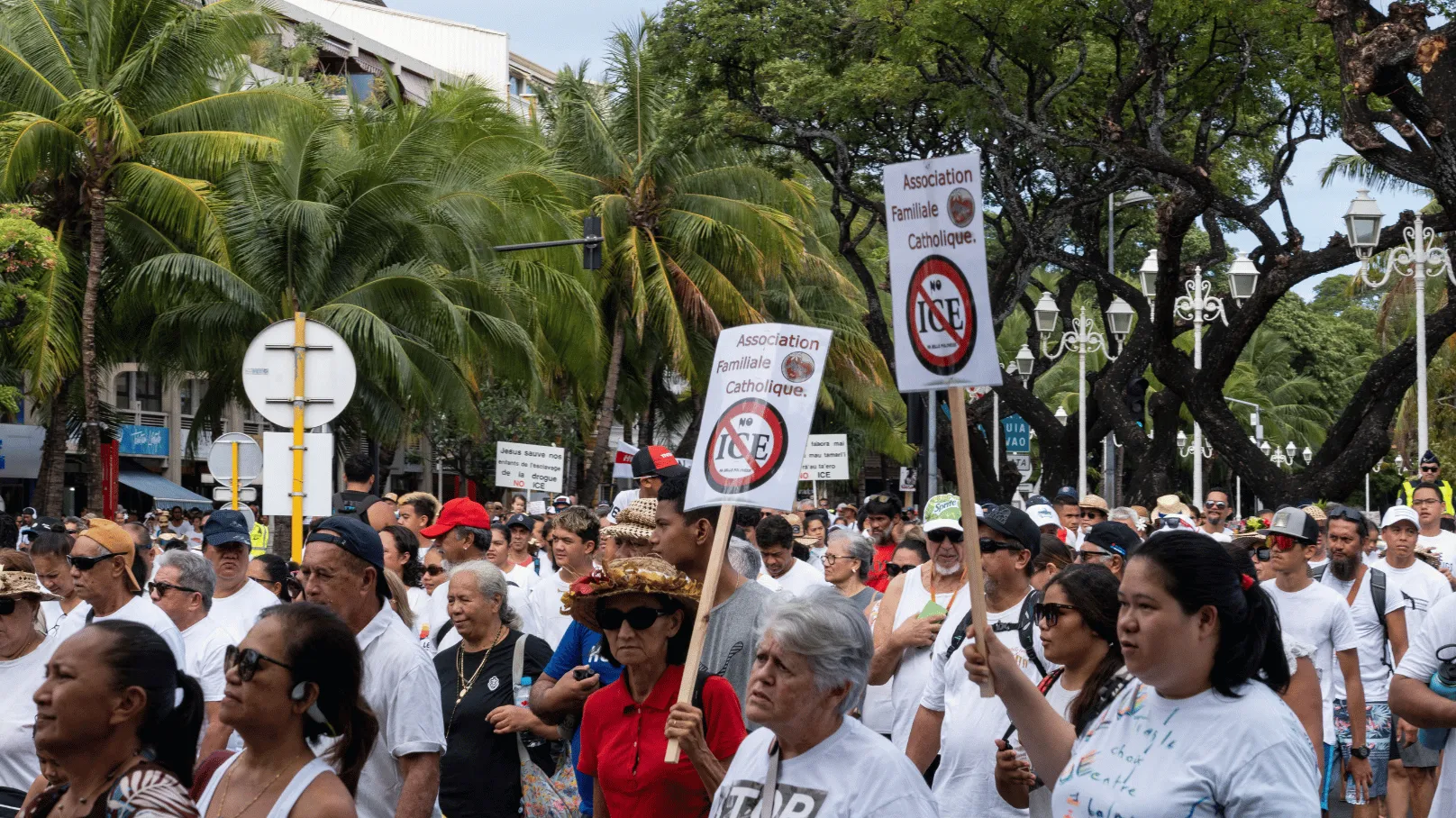 A large crowd marches through a tree-lined street in French Polynesia, with participants carrying signs opposing drug use and calling for drug prevention.